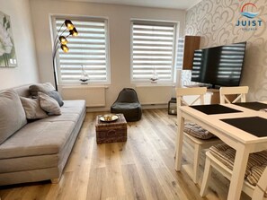 A modern living room with a sofa, a dining table, and a television. - 332 - Holiday Apartment 2 (Juist)