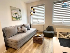 A modern living room with a grey sofa, a wicker side table, and a black armchair. - 332 - Holiday Apartment 2 (Juist)