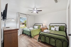 Ein Schlafzimmer mit zwei Betten, einem Schreibtisch, einem Deckenventilator und einem Fenster mit Vorhängen.