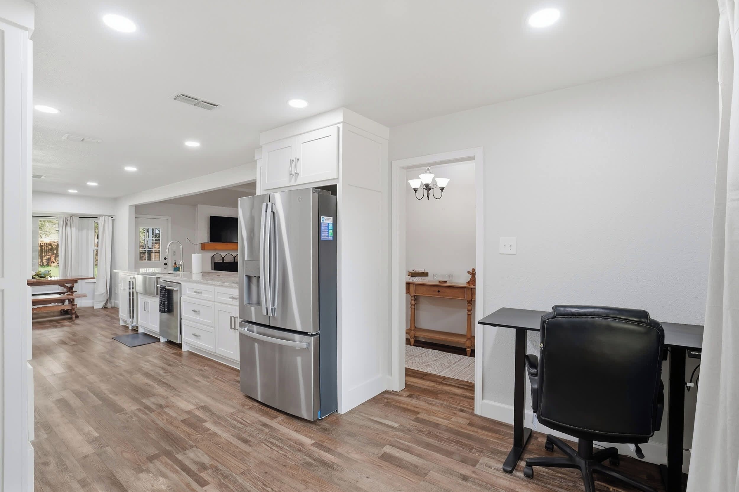 A modern kitchen with white cabinetry, a stainless steel refrigerator, and a dining area with a wooden table and chairs.