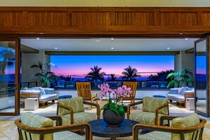 A modern outdoor seating area with a view of a sunset over the ocean, furnished with wicker chairs and a central table with a flower vase. - Wailea Beach | 2 Oceanfront Villas, Sleeps 14 | Car Incl. w/ 6+ Nights | ML-4274 by KBM (Wailea)
