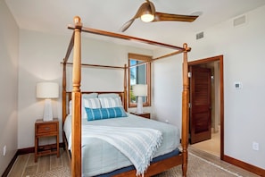 Ein Bett mit Baldachin, ein Deckenventilator, ein Nachttisch mit Lampe und ein Spiegel an der Wand.
