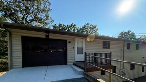 Ein eingeschossiges Gebäude mit Garage, einer kleinen Veranda und einer Treppe zu einer Terrasse.