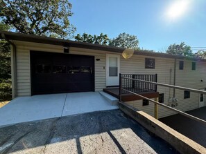 Ein eingeschossiges Gebäude mit Garage, einer kleinen Veranda und einer Treppe zu einer Terrasse.