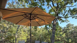 Eine Holzterrasse mit Tisch und Stühlen unter einem großen Sonnenschirm.