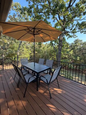 Eine Holzterrasse mit Tisch und Stühlen unter einem großen Sonnenschirm.