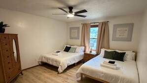 Ein Schlafzimmer mit zwei Betten, einem Deckenventilator, einer Holzkommode und einem Fenster mit Vorhängen.