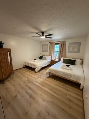 Ein Schlafzimmer mit zwei Betten, einem Deckenventilator, einer Holzkommode und einem Fenster mit Vorhängen.