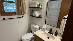 Ein Badezimmer mit Toilette, Waschbecken, Spiegel, Handtuchhalter und einem Fenster mit Vorhängen.
