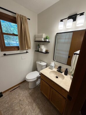 Ein Badezimmer mit Toilette, Waschbecken, Spiegel, Handtuchhalter und einem Fenster mit Vorhängen.