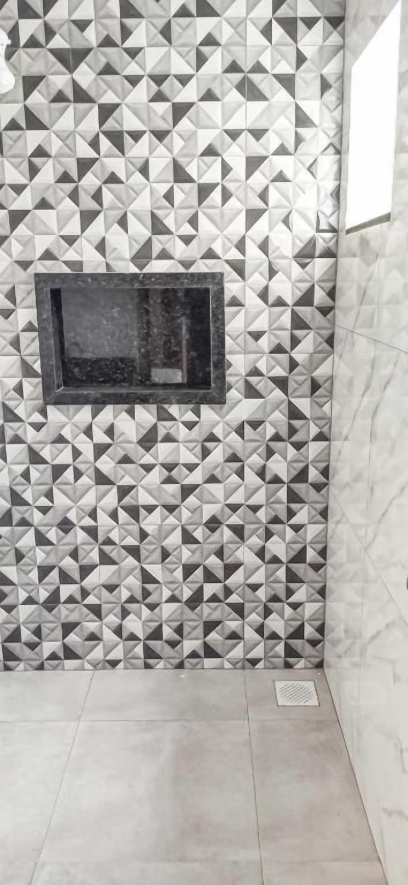 Casa de banho com parede de padrão geométrico, uma pequena janela e chão em mosaico.