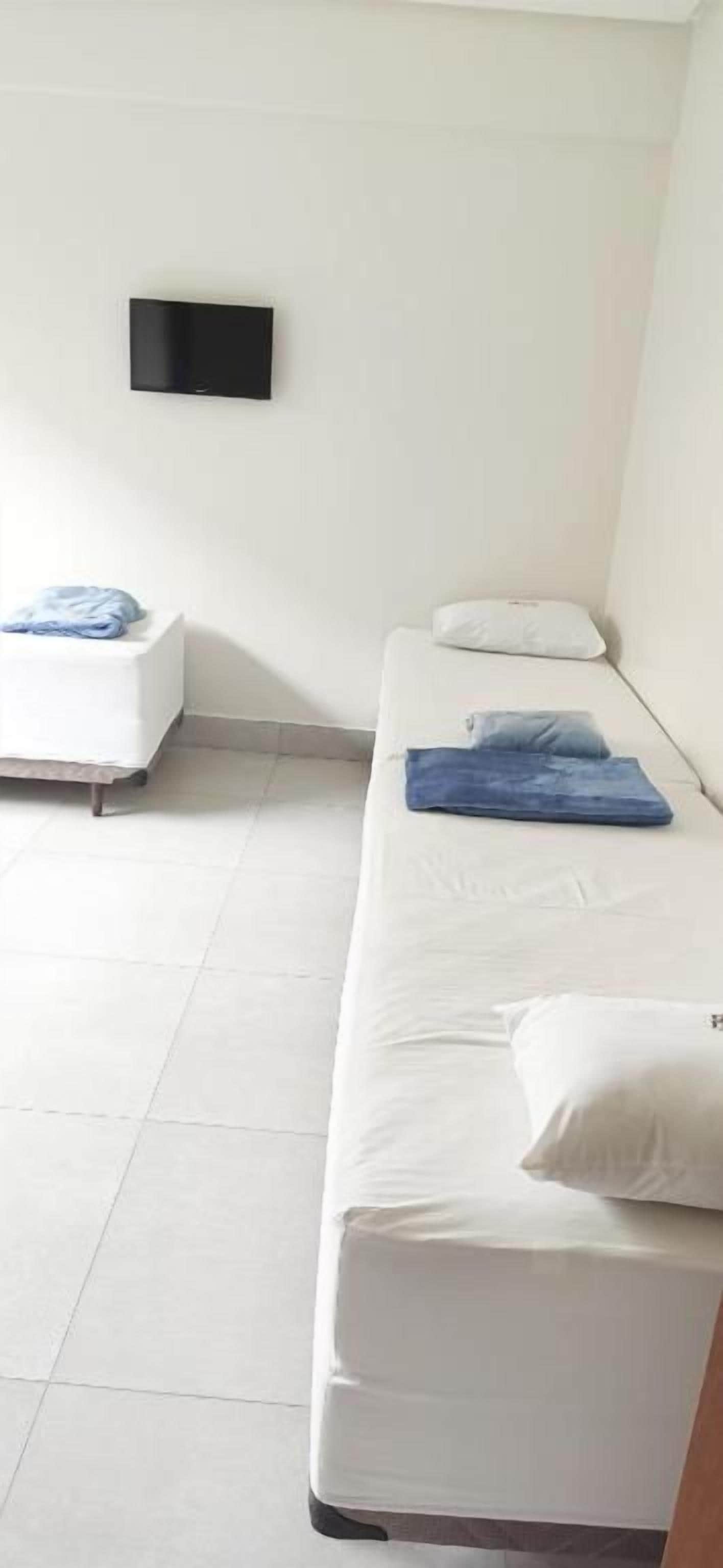 Quarto com cama, uma mesinha e televisão fixada na parede.