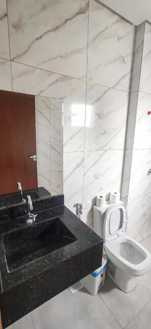 Un baño con un lavabo negro, inodoro blanco y paredes de mármol.