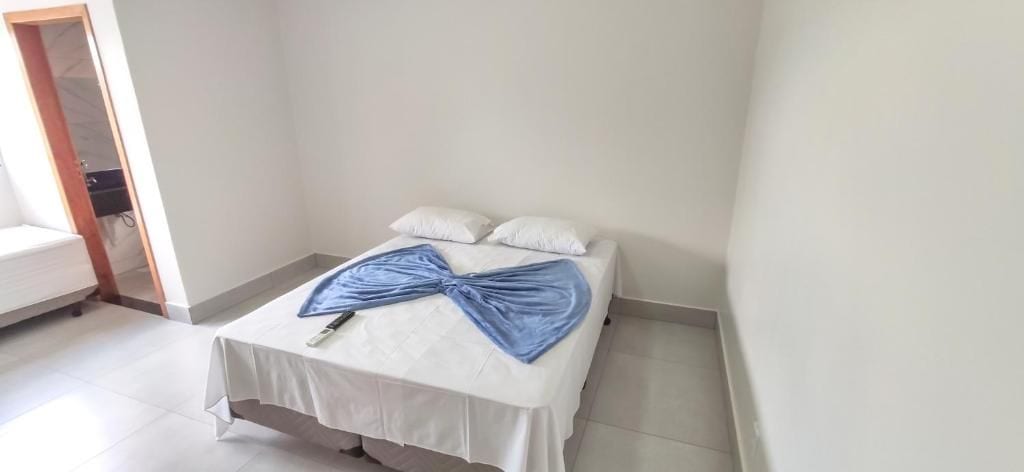 A single bed with white bedding and a blue accent, a white wall, and a door leading to another room.