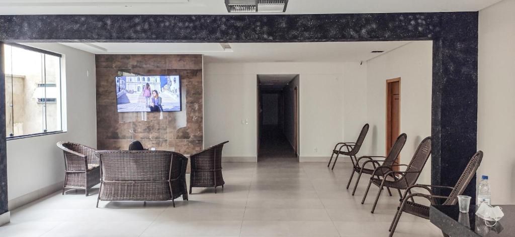 Um saguão de hotel com uma TV de tela plana fixada em uma parede de pedra, cadeiras de vime dispostas para acomodar hóspedes, e vista desobstruída para o corredor.