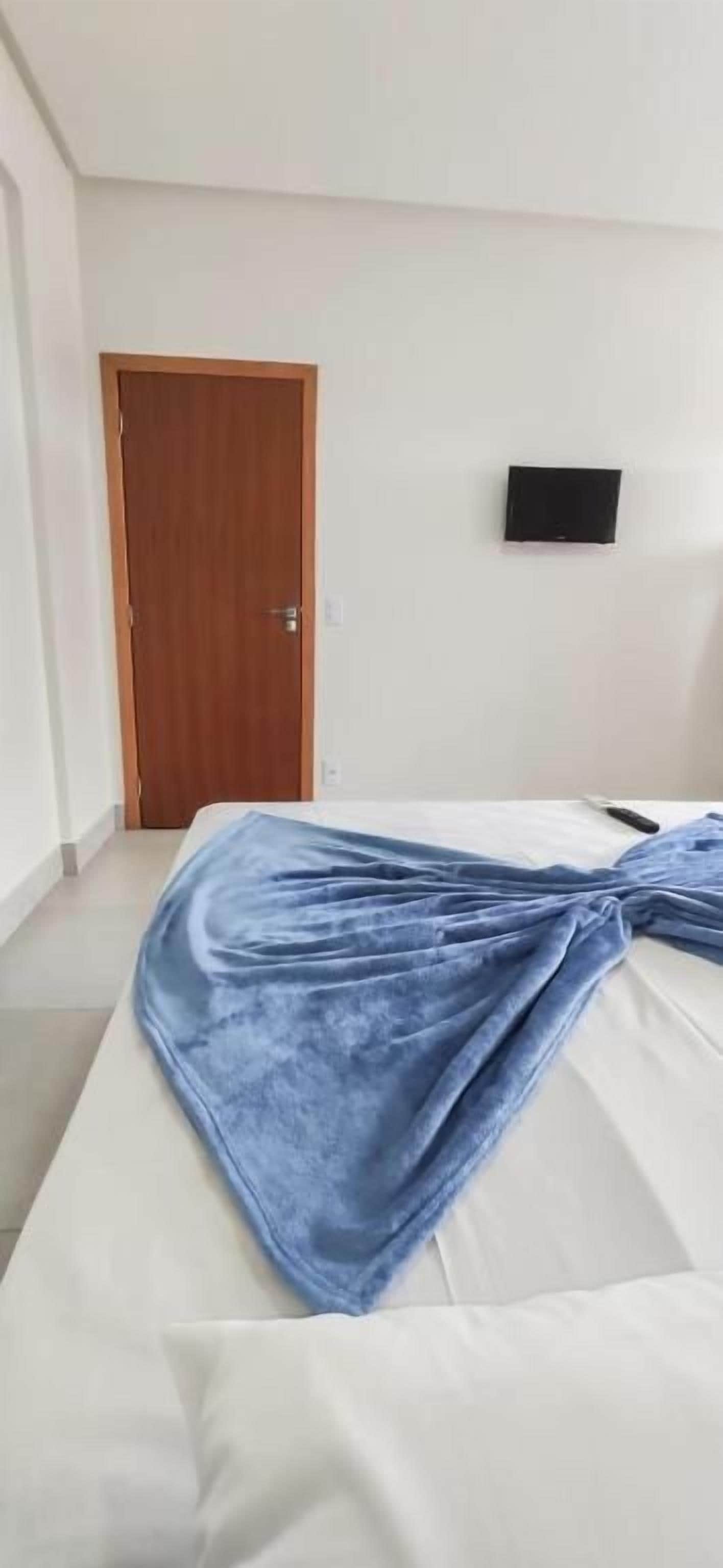 A hotel room with a bed, a wooden door, and a flat-screen TV on the wall.