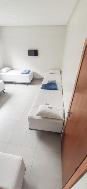 Habitación de hotel con dos camas, una puerta de madera y un objeto negro pequeño en la pared.