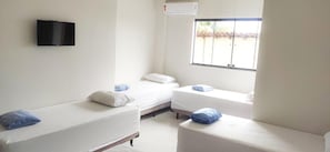 A room with two single beds, a flat-screen TV mounted on the wall, and a window with a view of the outside. - Hotel Turismo  (Trindade)
