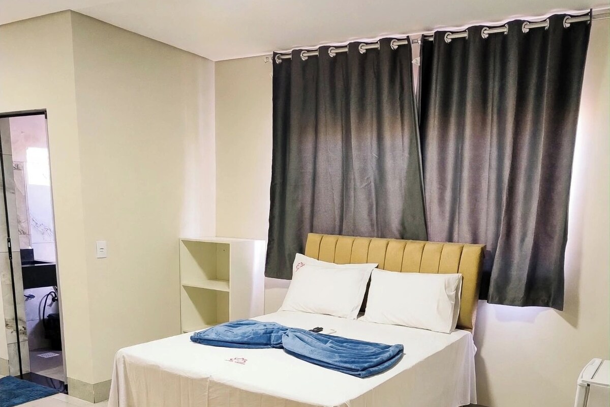 Habitación de hotel con cama, mesita de noche, lámpara, ventana con cortinas y una alfombra estampada.