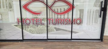 Entrada de un hotel con puerta de cristal que muestra el nombre del hotel 'HOTEL TURISMO' y un logotipo estilizado.