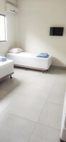 Quarto com cama, uma pequena mesa e televisão na parede.