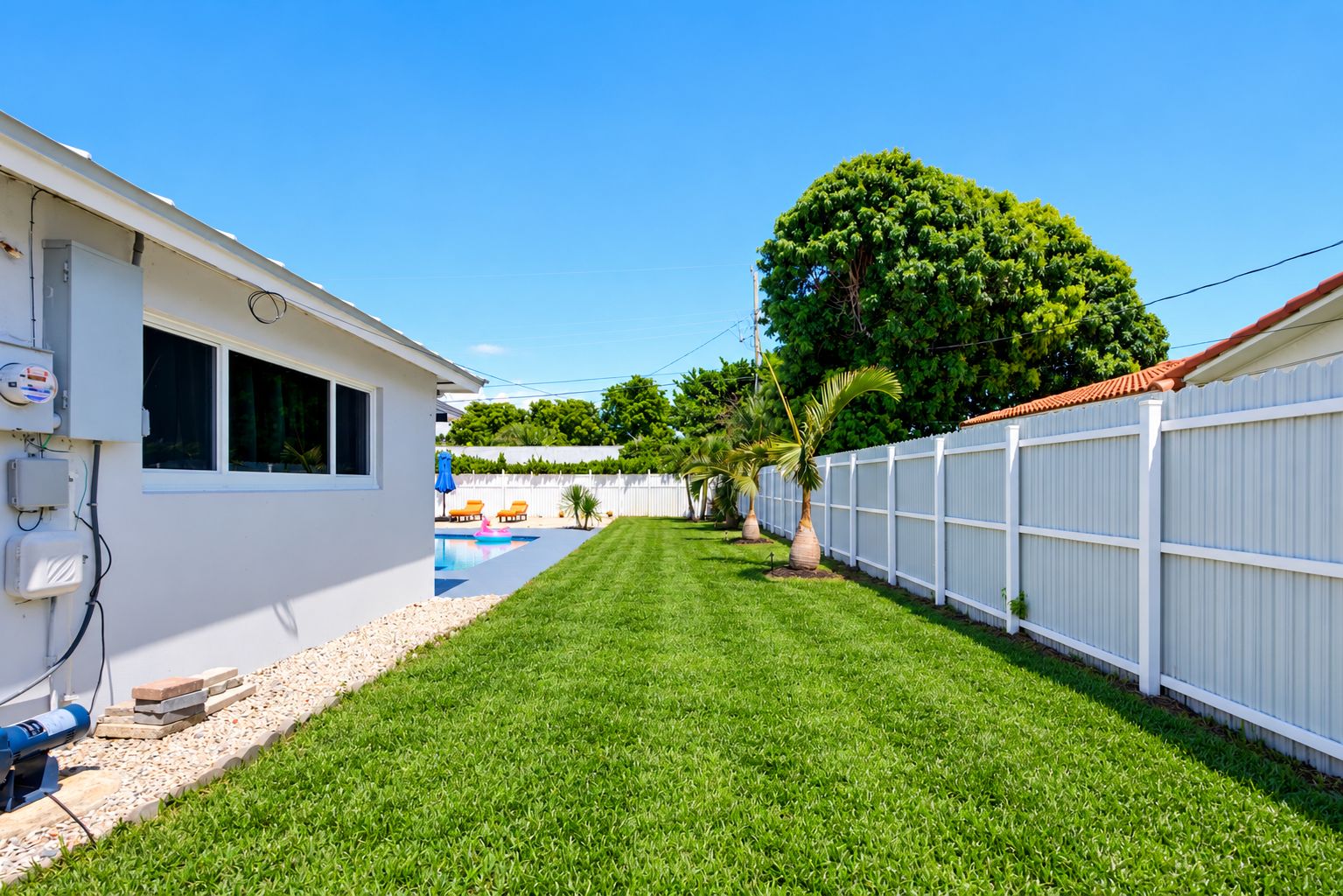 A residential backyard with a swimming pool, a white fence, and a tree.