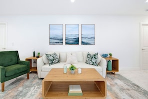 A modern living room with a sofa, a green armchair, a coffee table, and three wall-mounted paintings. - Our Caribbean Home (West Palm Beach)