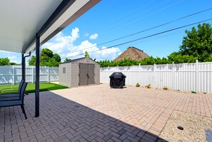A covered patio area with a brick floor, a white fence, and a small shed. - Our Caribbean Home (West Palm Beach)