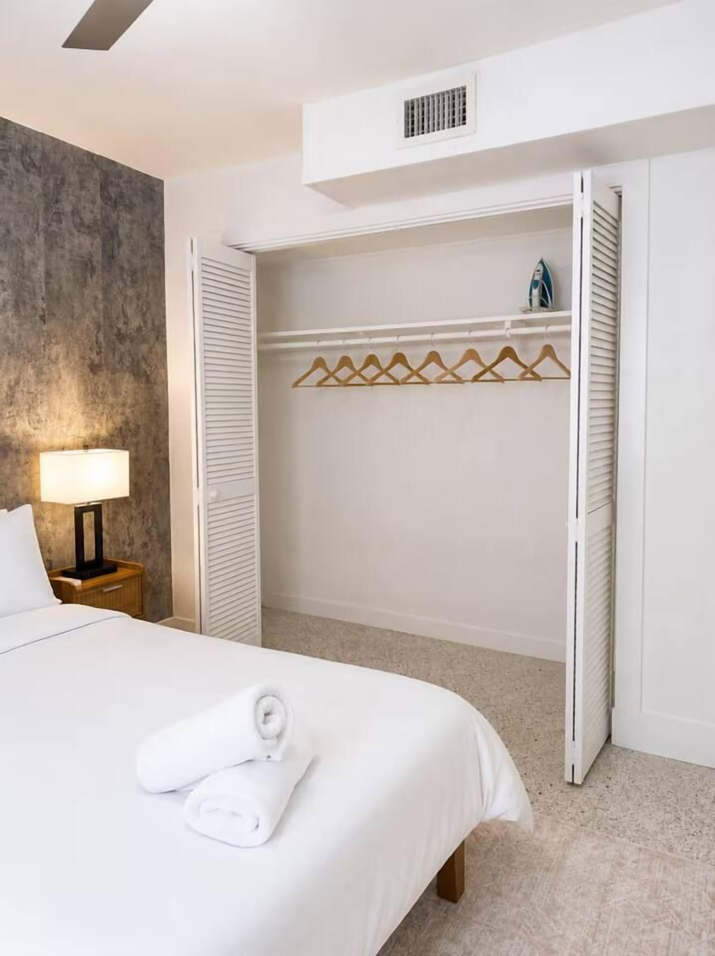 Une chambre d’hôtel avec un lit, une table de chevet, une lampe, une armoire avec une tringle pour suspendre les vêtements et une serviette sur le lit.