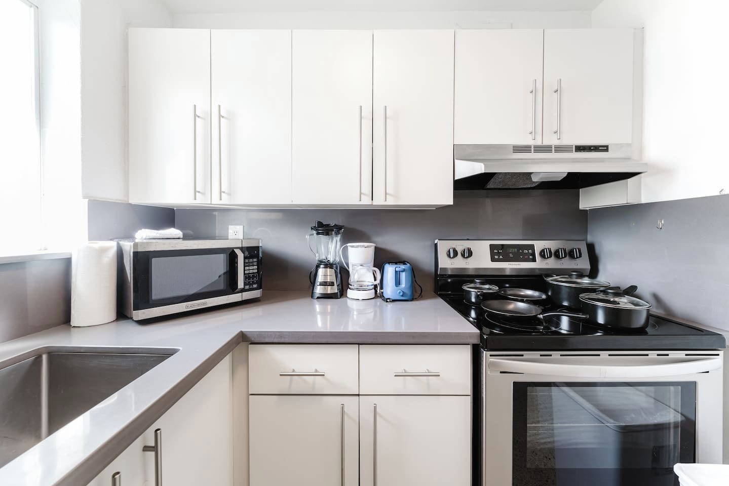 A modern kitchen with white cabinets, a microwave, a stove, and a coffee maker.