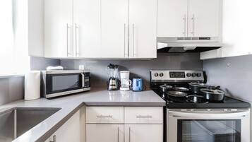 A modern kitchen with white cabinets, a microwave, a stove, and a coffee maker.