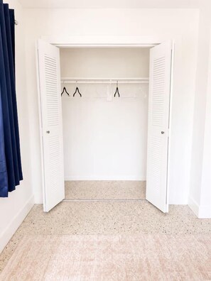 Un placard blanc, dont les portes sont ouvertes, avec une tringle à vêtements et un sol à motifs.