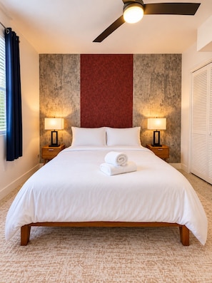 A hotel room with a large bed, two bedside lamps, a ceiling fan, and a red accent wall. - 5-Star Location | Heart of Wynwood 2BR+Parking (Miami)
