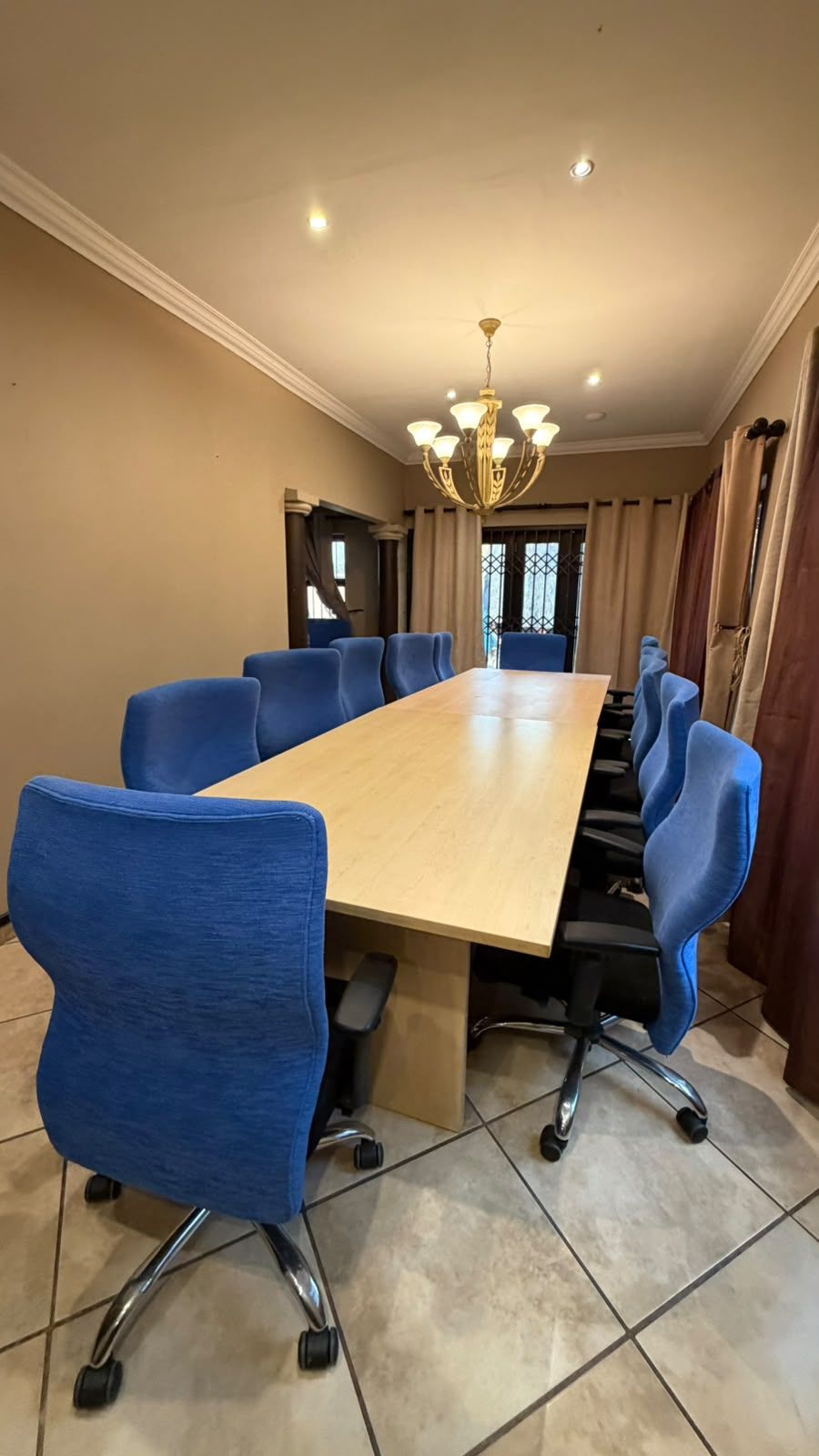 Una sala conferenze con un lungo tavolo, sedie blu, un lampadario e vista dalla finestra.