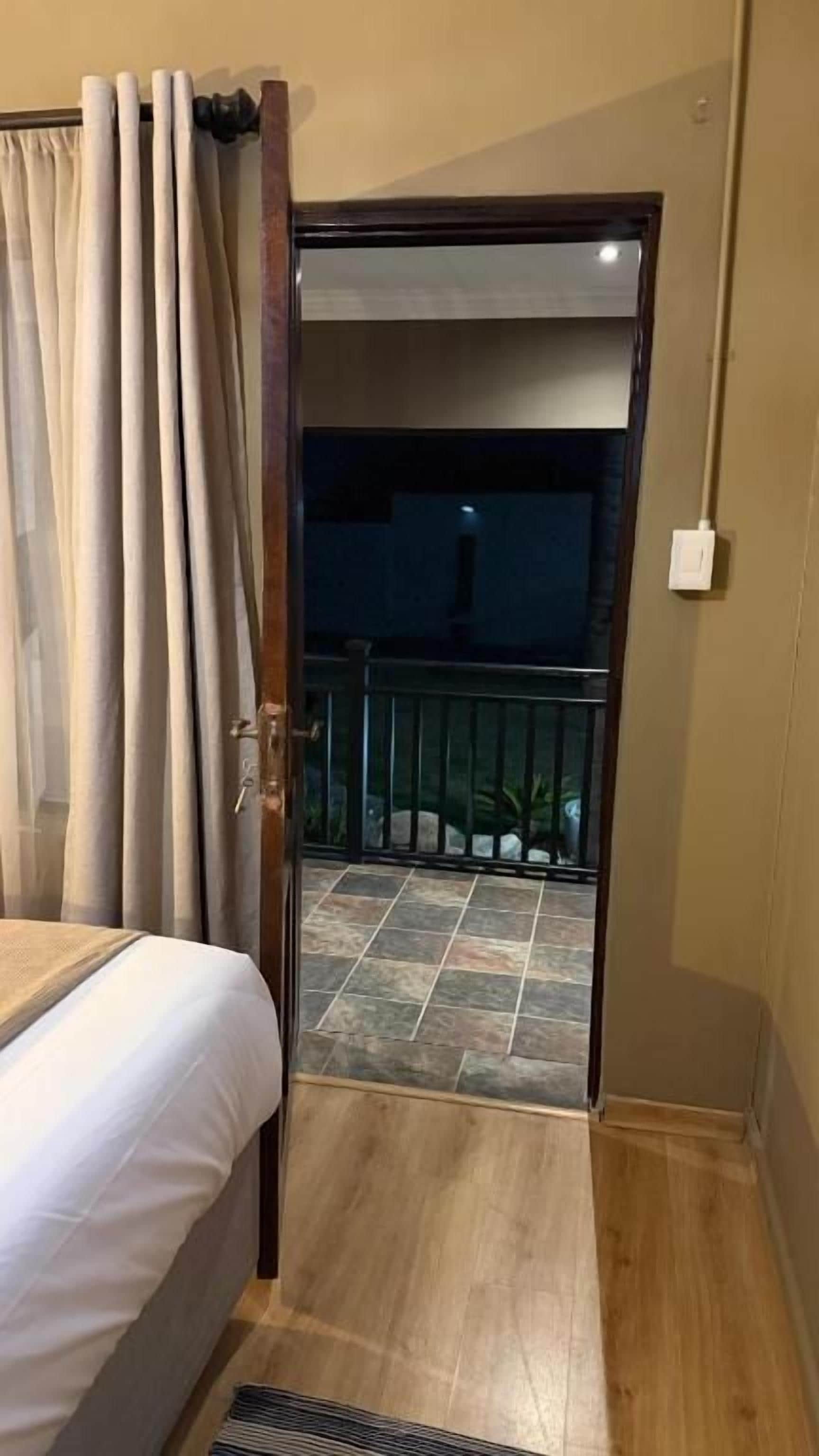 A bedroom with a bed, a door leading to a balcony, and a visible outdoor area with a railing.