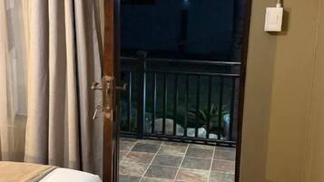 A bedroom with a bed, a door leading to a balcony, and a visible outdoor area with a railing.