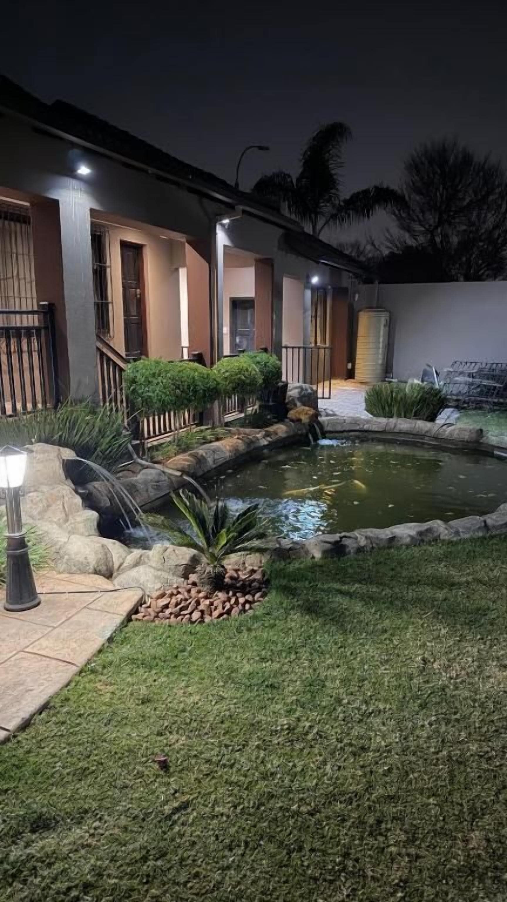 Un área exterior bien cuidada con un pequeño estanque, un sendero y un edificio con varias ventanas y puertas.