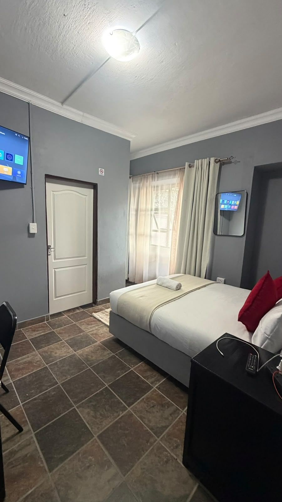 Habitación de hotel con una cama, televisor montado en la pared, una puerta y una ventana con cortinas.