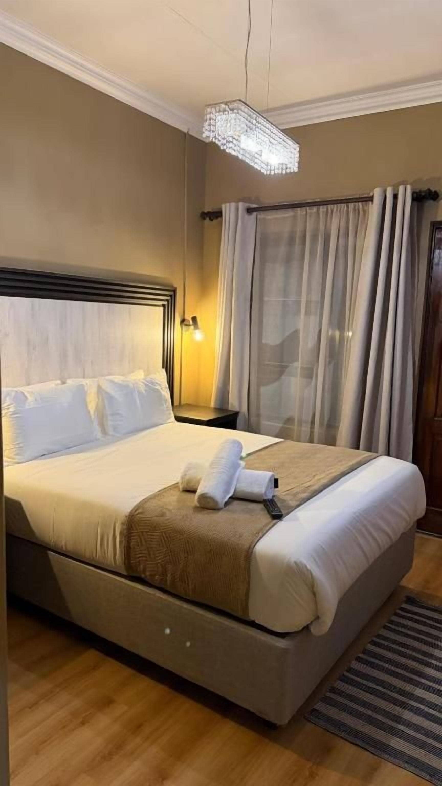 A hotel room with a bed, a nightstand, a lamp, and a window with curtains.