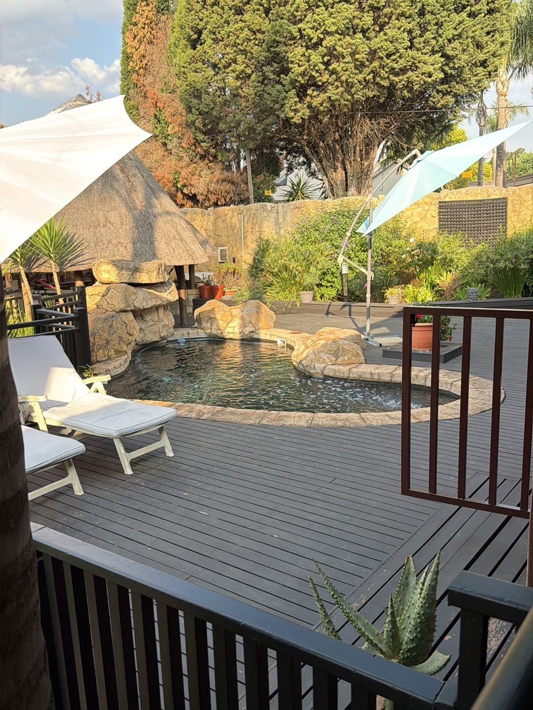 Une terrasse en bois avec une piscine, entourée de rochers et de plantes.