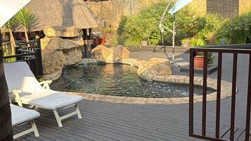 Une terrasse en bois avec une piscine, entourée de rochers et de plantes.