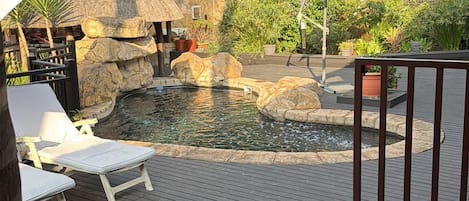 Una terraza de madera con piscina, rodeada de rocas y plantas.