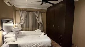 Une chambre d’hôtel avec deux lits, une armoire, un ventilateur de plafond et un sol recouvert de moquette.