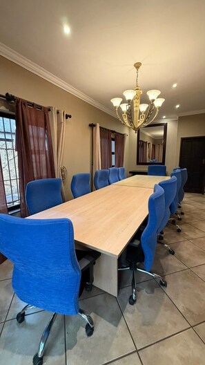 Un salón de conferencias con una larga mesa y sillas azules, una araña y cortinas en las ventanas.