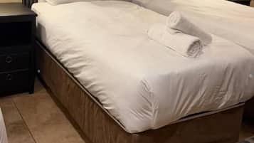 Una cama bien hecha con ropa blanca y una toalla doblada, una mesita de noche y un equipo de aire acondicionado instalado en la pared.