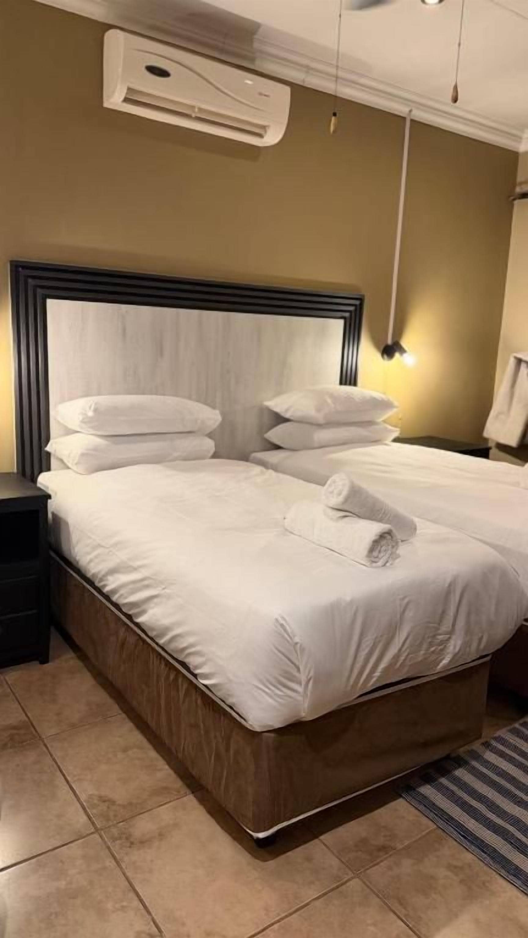 Habitación de hotel con una cama grande, una mesita de noche, un aire acondicionado y una lámpara.