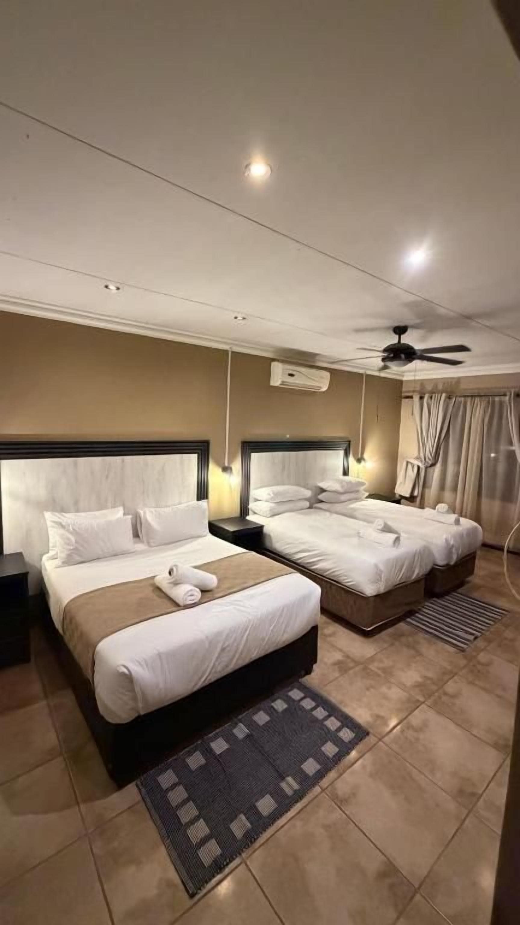 Een hotelkamer met twee bedden, een plafondventilator en een raam met gordijnen.