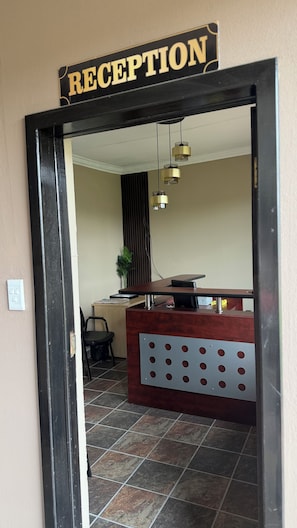 Una zona de recepción con un cartel sobre la puerta, un mostrador, sillas y una planta.