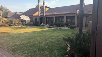 Um imóvel residencial com calçada pavimentada, gramado e palmeiras.