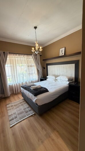 Un dormitorio con cama, mesitas de noche, candelabro, ventana con cortinas y alfombra.